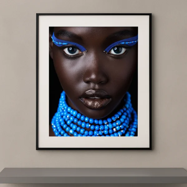 Portrait artistique de beauté ethnique avec maquillage bleu graphique, colliers de perles bleues et regard intense sur fond noir.