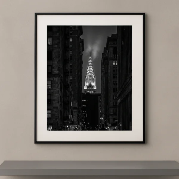 Tableau noir et blanc du Chrysler Building illuminé entre les immeubles de Manhattan