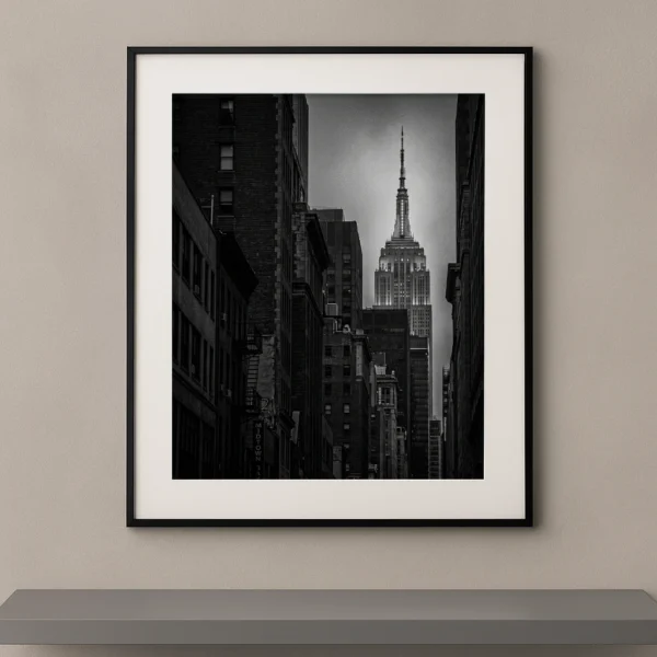 Tableau noir et blanc de l’Empire State Building encadré par les immeubles de Manhattan