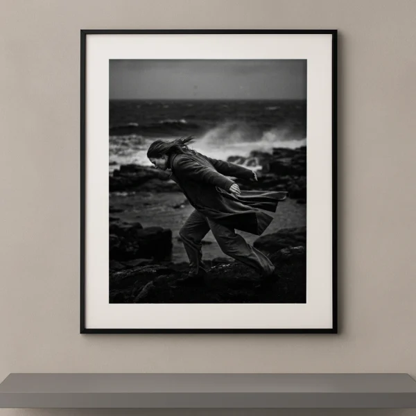 Tableau noir et blanc d'une silhouette avançant contre le vent sur une côte sauvage