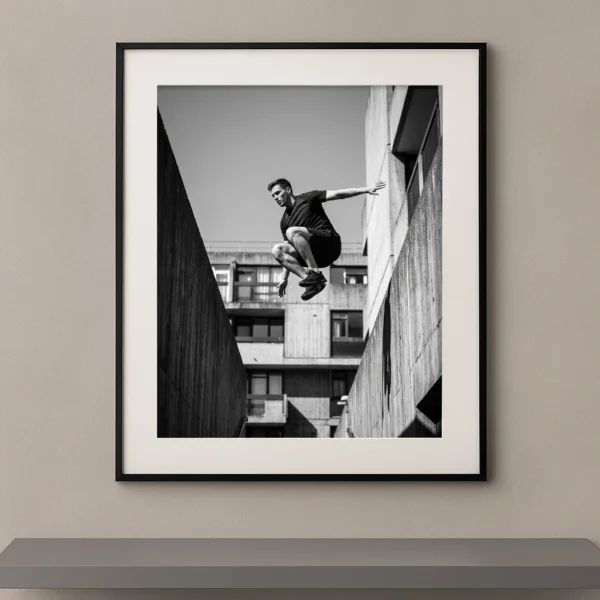 Tableau noir et blanc d’un athlète de parkour en plein saut entre deux structures urbaines