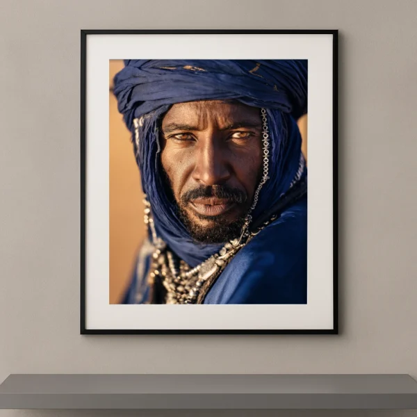 Portrait Fine Art d'un homme nomade du Sahara portant un voile bleu traditionnel et des bijoux sahariens sous la lumière dorée du désert.