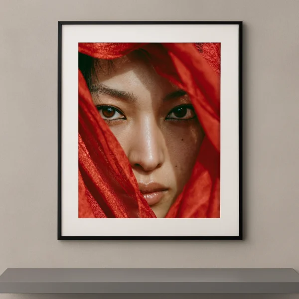 Portrait artistique d'une femme au regard intense apparaissant derrière un voile rouge lumineux dans un style photographique contemporain.