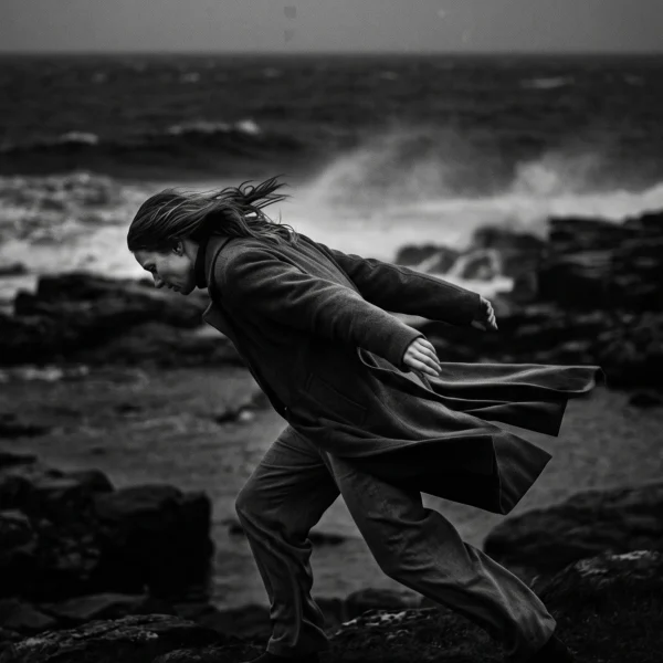 Face au Vent — silhouette avançant sur une côte battue par les vents, manteau et mer agitée, photographie noir et blanc, art mural premium