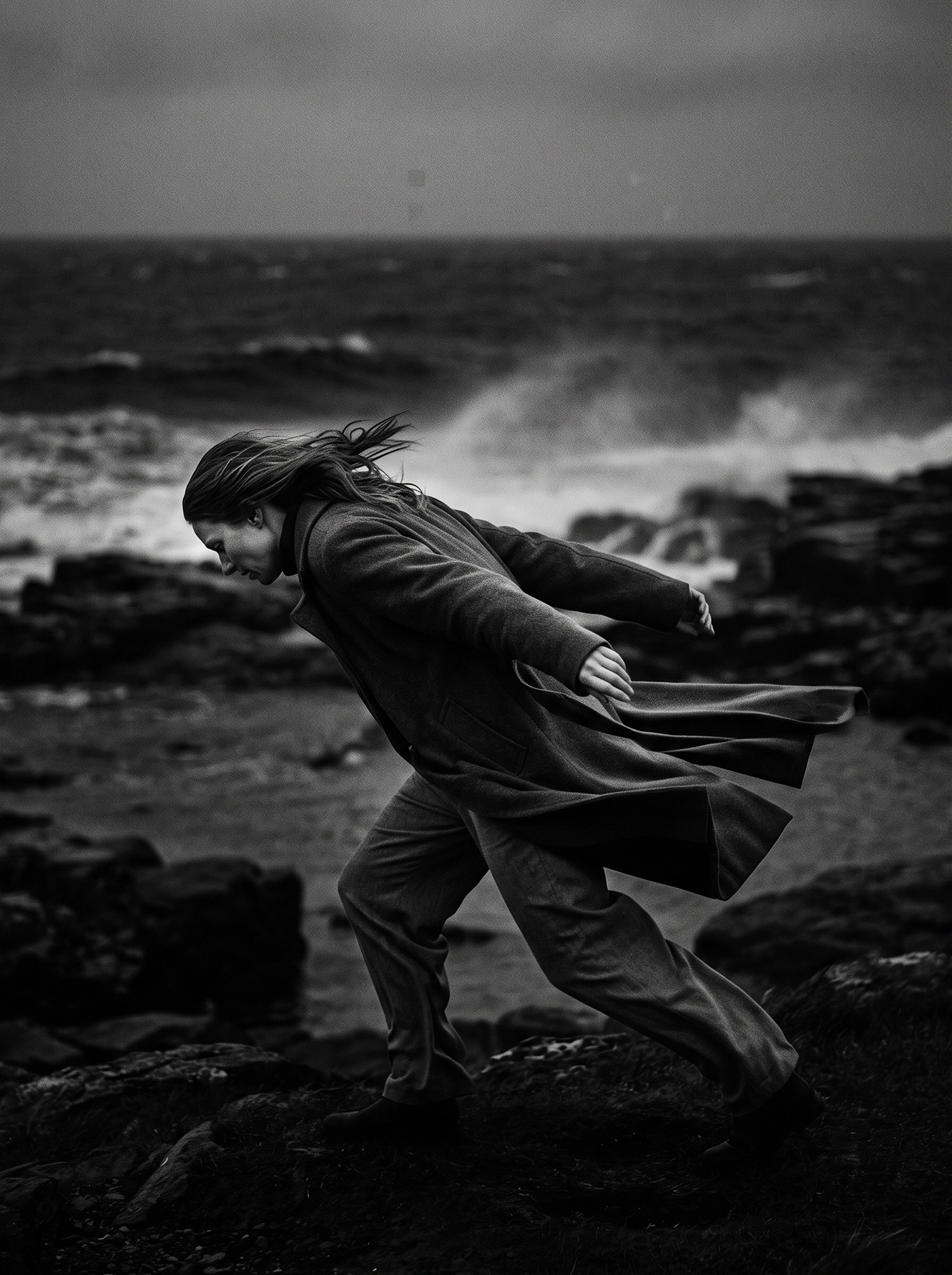 Face au Vent — silhouette avançant sur une côte battue par les vents, manteau et mer agitée, photographie noir et blanc, art mural premium