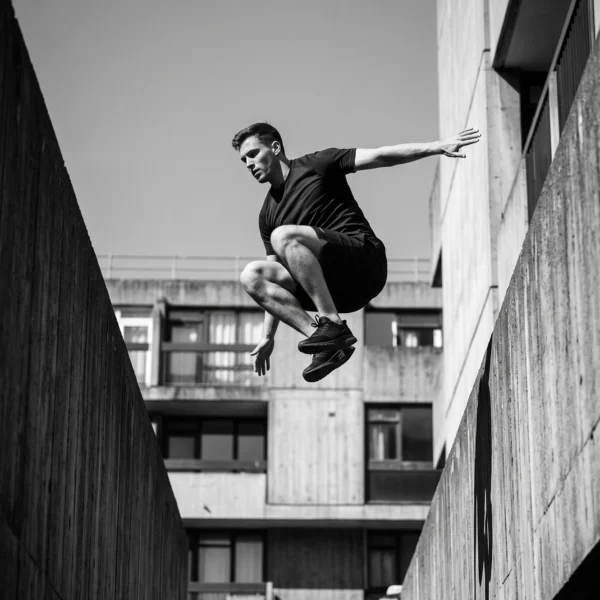 L'Élan — athlète de parkour suspendu entre deux structures de béton, photographie noir et blanc, art mural premium