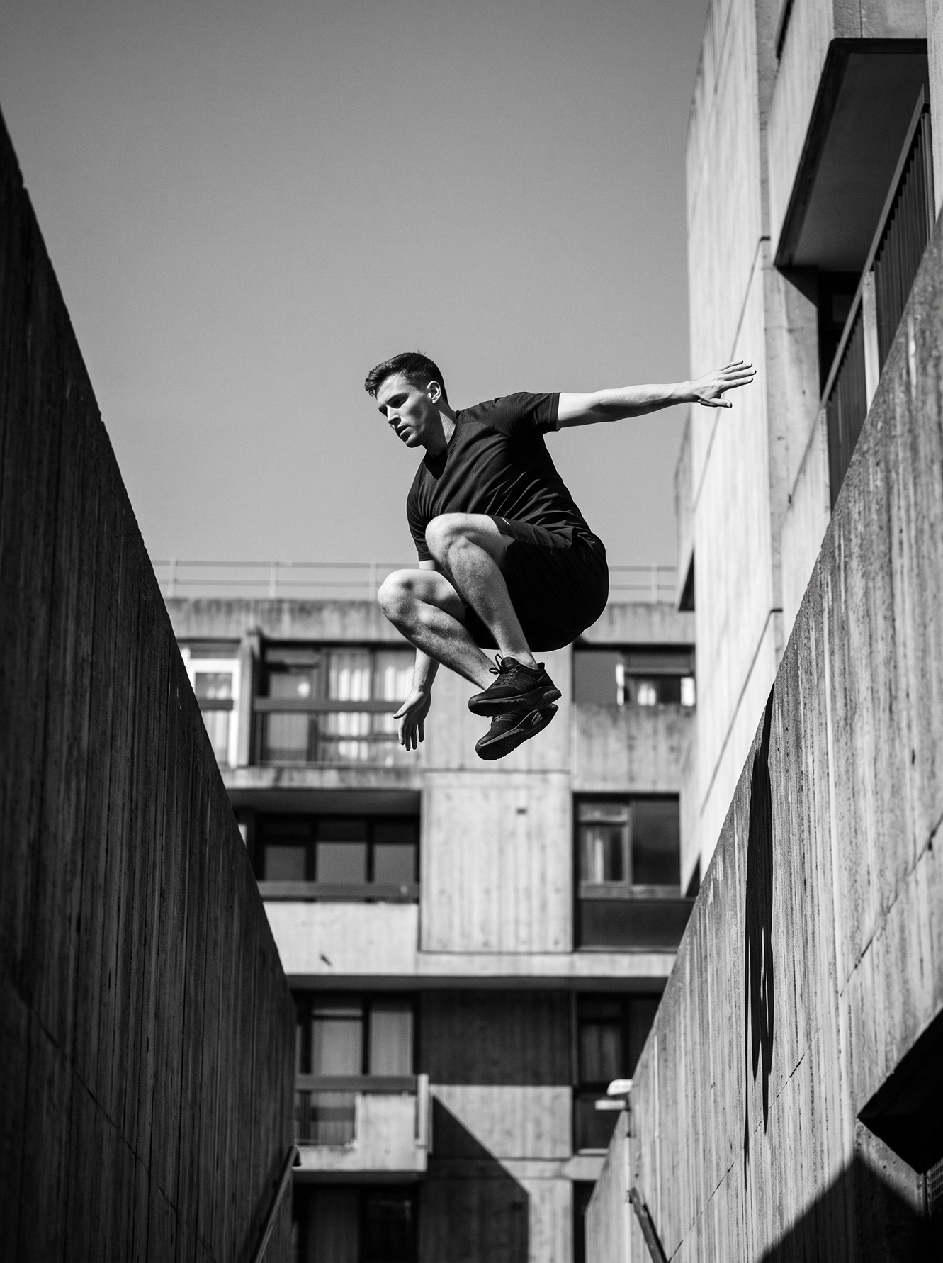 L'Élan — athlète de parkour suspendu entre deux structures de béton, photographie noir et blanc, art mural premium