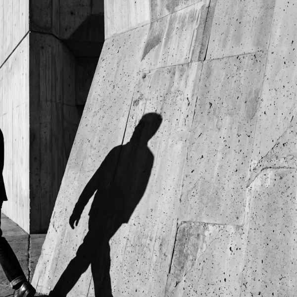 Le Passant — ombre d'une silhouette en marche sur un mur de béton, photographie graphique noir et blanc, art mural premium