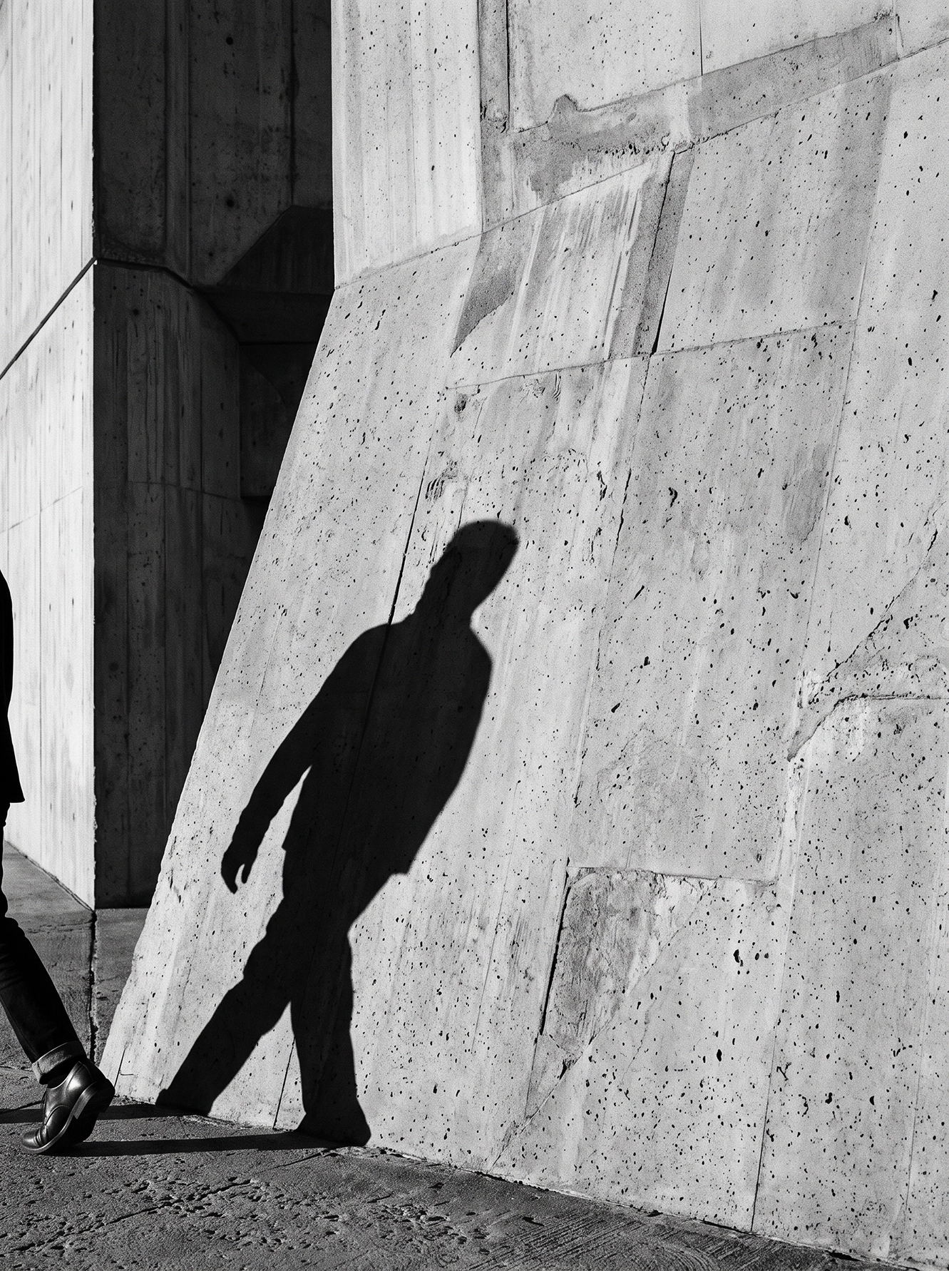 Le Passant — ombre d'une silhouette en marche sur un mur de béton, photographie graphique noir et blanc, art mural premium