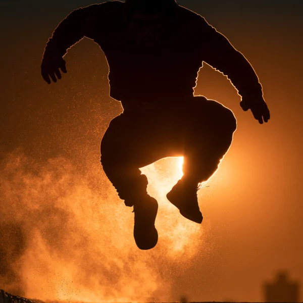 Parkour — silhouette athlétique en plein vol au-dessus d'un toit urbain, coucher de soleil orangé, art mural premium